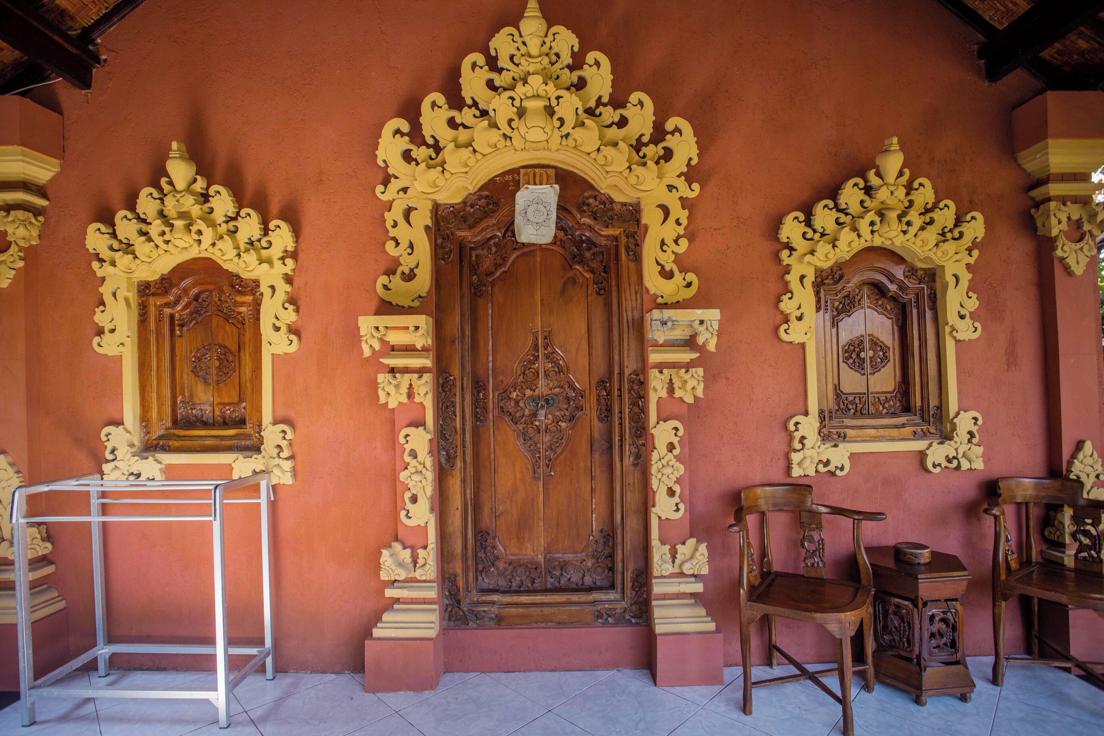 Une porte en bois traditionnelle, ornée de sculptures complexes, flanquée de deux portes plus petites aux motifs similaires, et une étagère en métal placée devant.