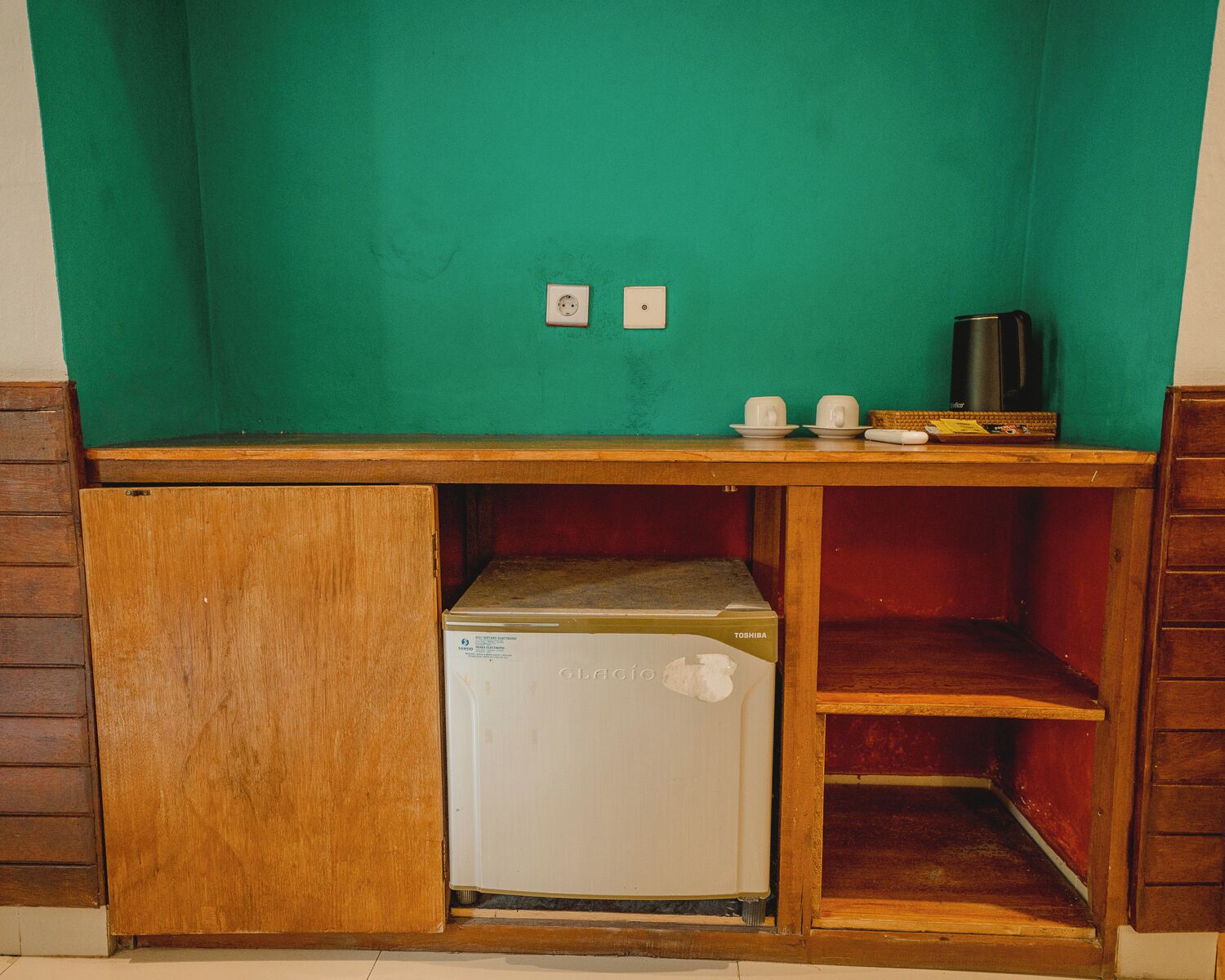 Eine kompakte Küchenzeile mit Kühlschrank, Mikrowelle, Toaster und einer kleinen Kaffeemaschine auf einer Holzausziehtafel.