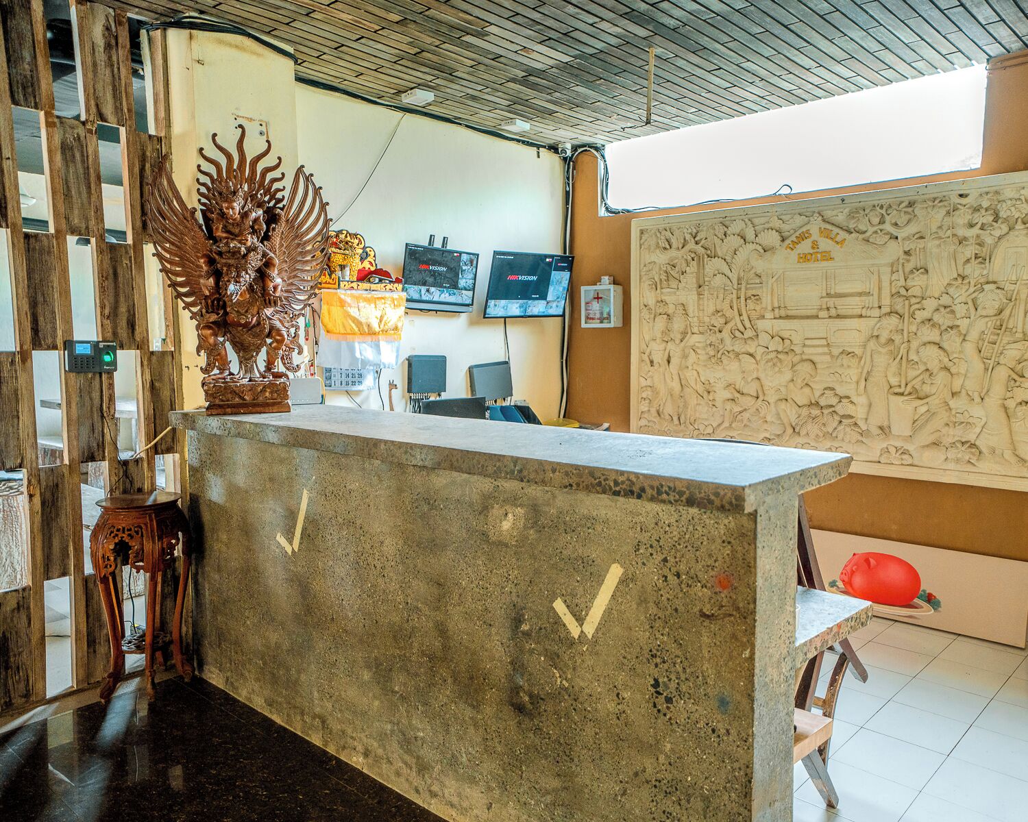 A reception desk with a decorative wooden sculpture, a wall-mounted TV, and a large carved relief artwork.
