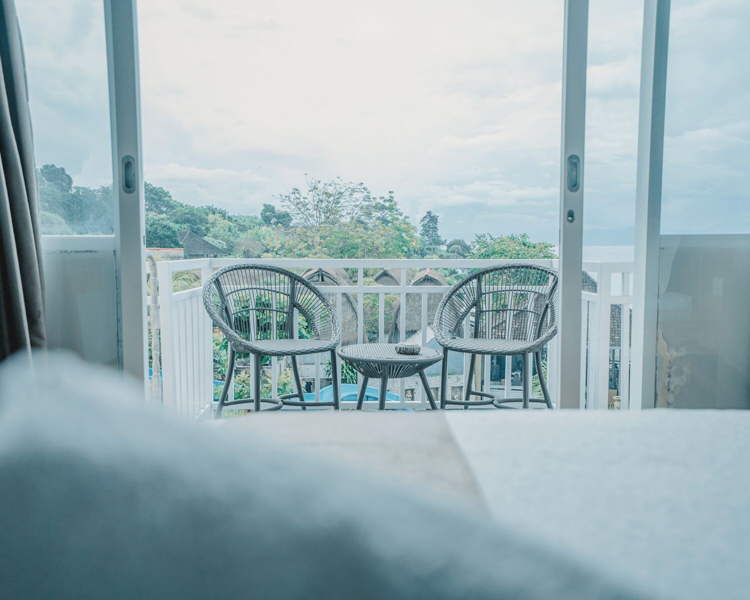 A balcony with two wicker chairs and a small table, overlooking a lush green landscape.