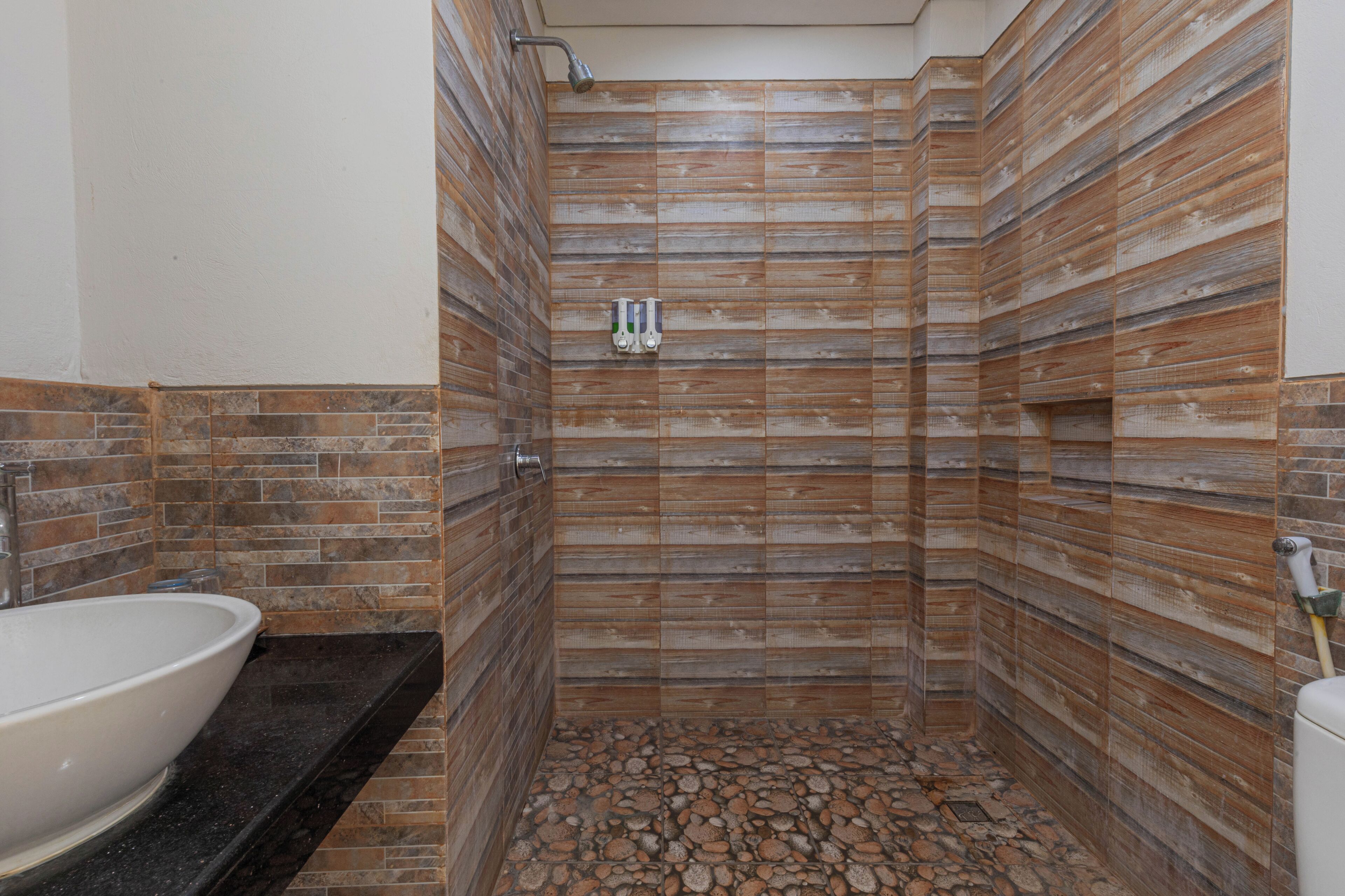 Une salle de bain avec un lavabo blanc, une douche aux parois revêtues de panneaux en bois et un sol carrelé de pierres.