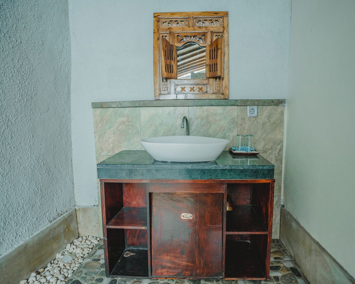 Un baño con un lavamanos blanco tipo pedestal, un mueble de tocador de madera y un espejo con detalles decorativos.