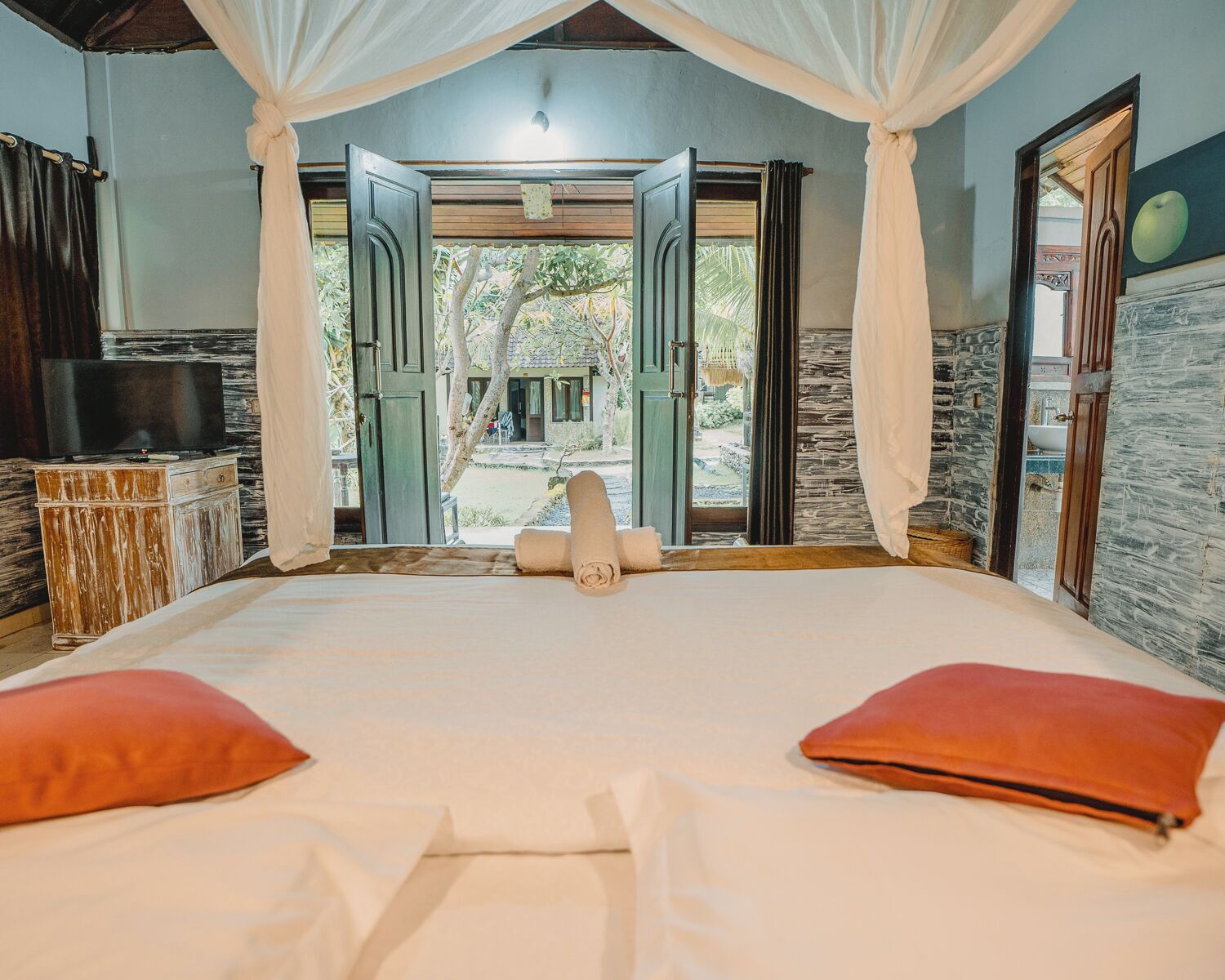 Un dormitorio con una cama grande, cortinas blancas y vistas a un jardín.