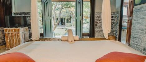 Un dormitorio con una cama grande, cortinas blancas y vistas a un jardín.