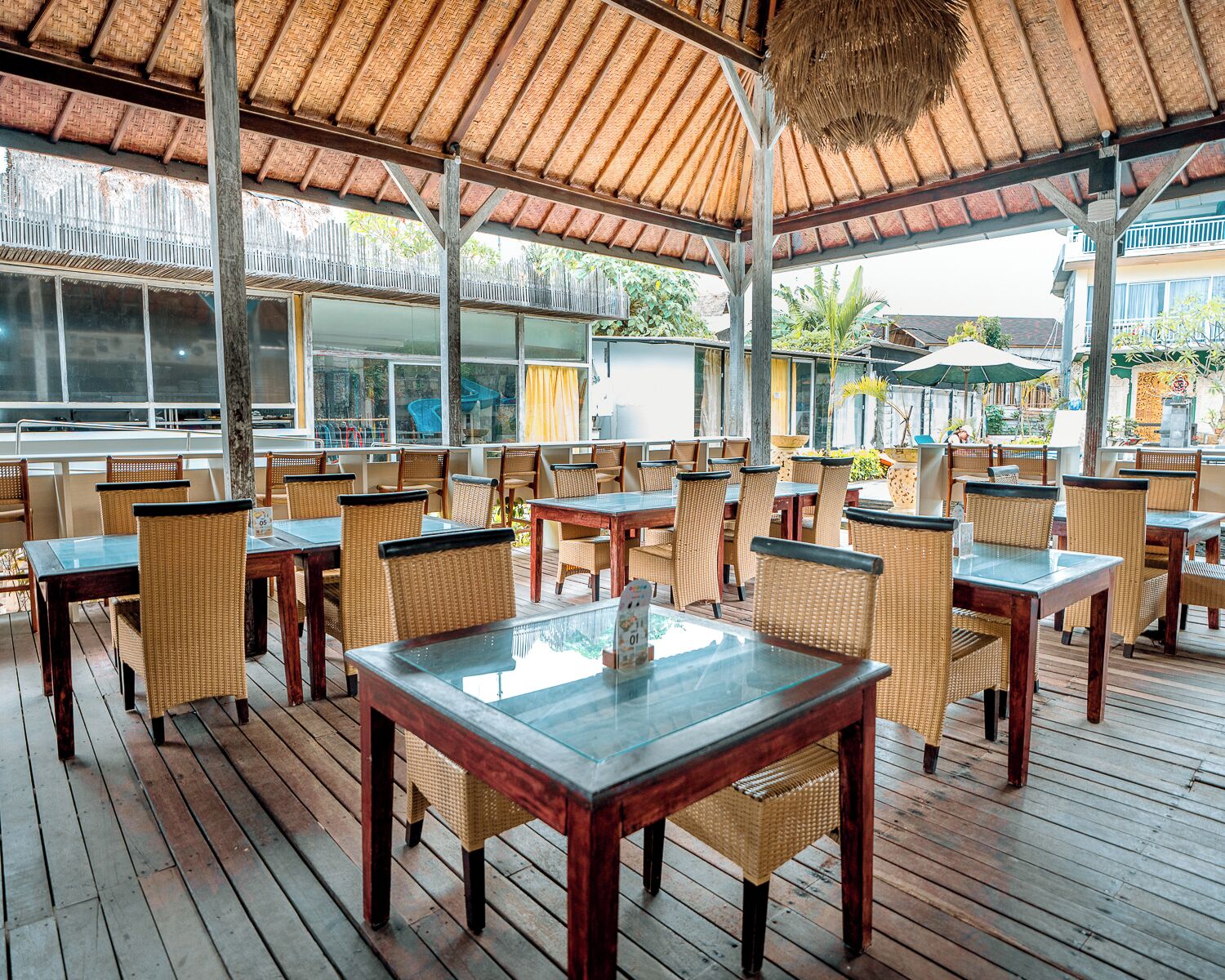 Un restaurante al aire libre con mesas de madera y sillas de mimbre, techo de paja y vistas del entorno.