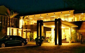 L’entrée d’un hôtel, avec une voiture garée devant, de grandes colonnes et des plantes en pot.