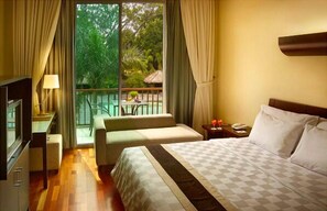 Une chambre d’hôtel avec un lit, une télévision, un balcon avec une table et des chaises, et une vue sur la verdure environnante.