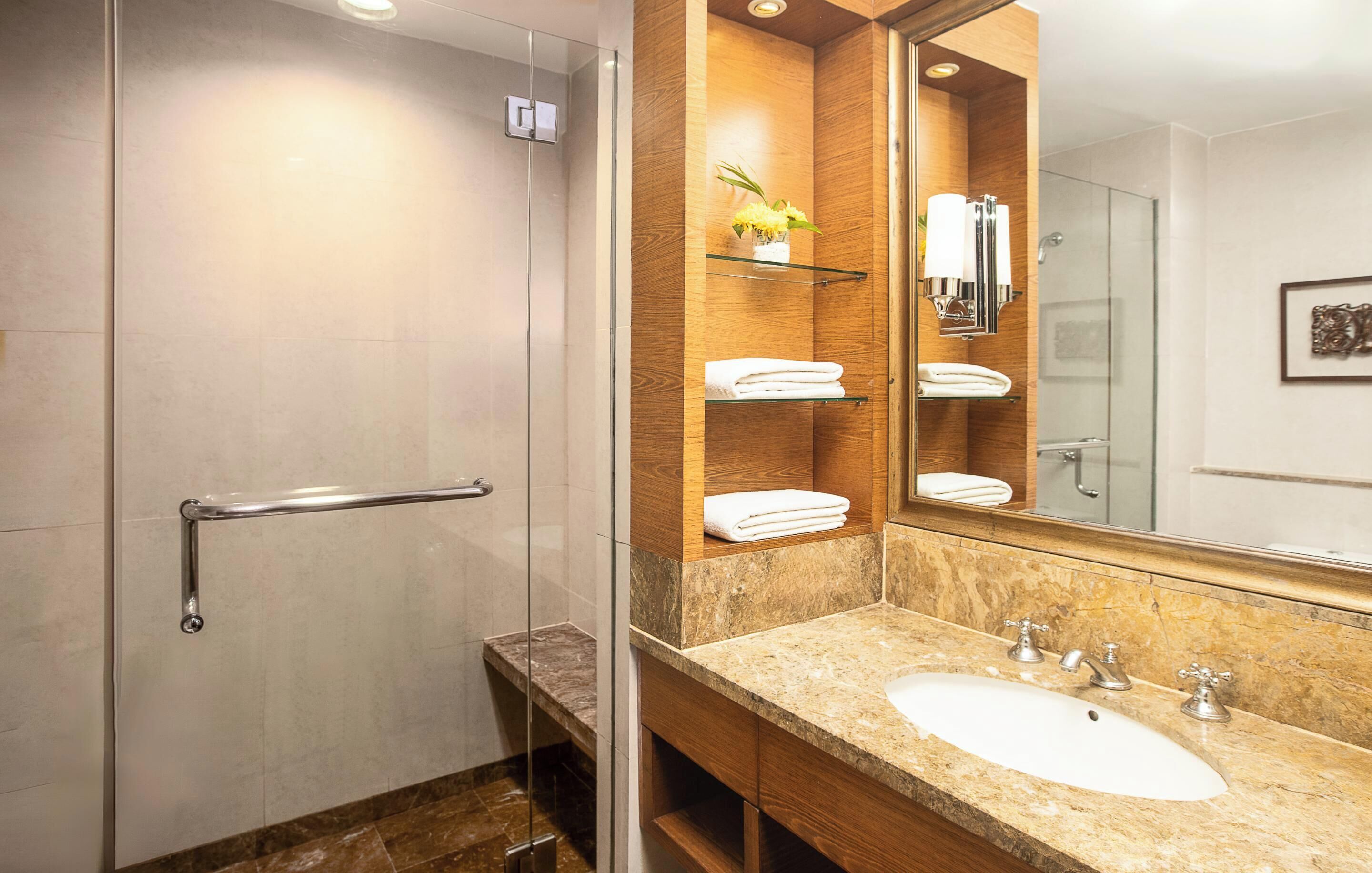 A modern bathroom with a glass shower enclosure, a marble sink, and a wooden vanity with a mirror.