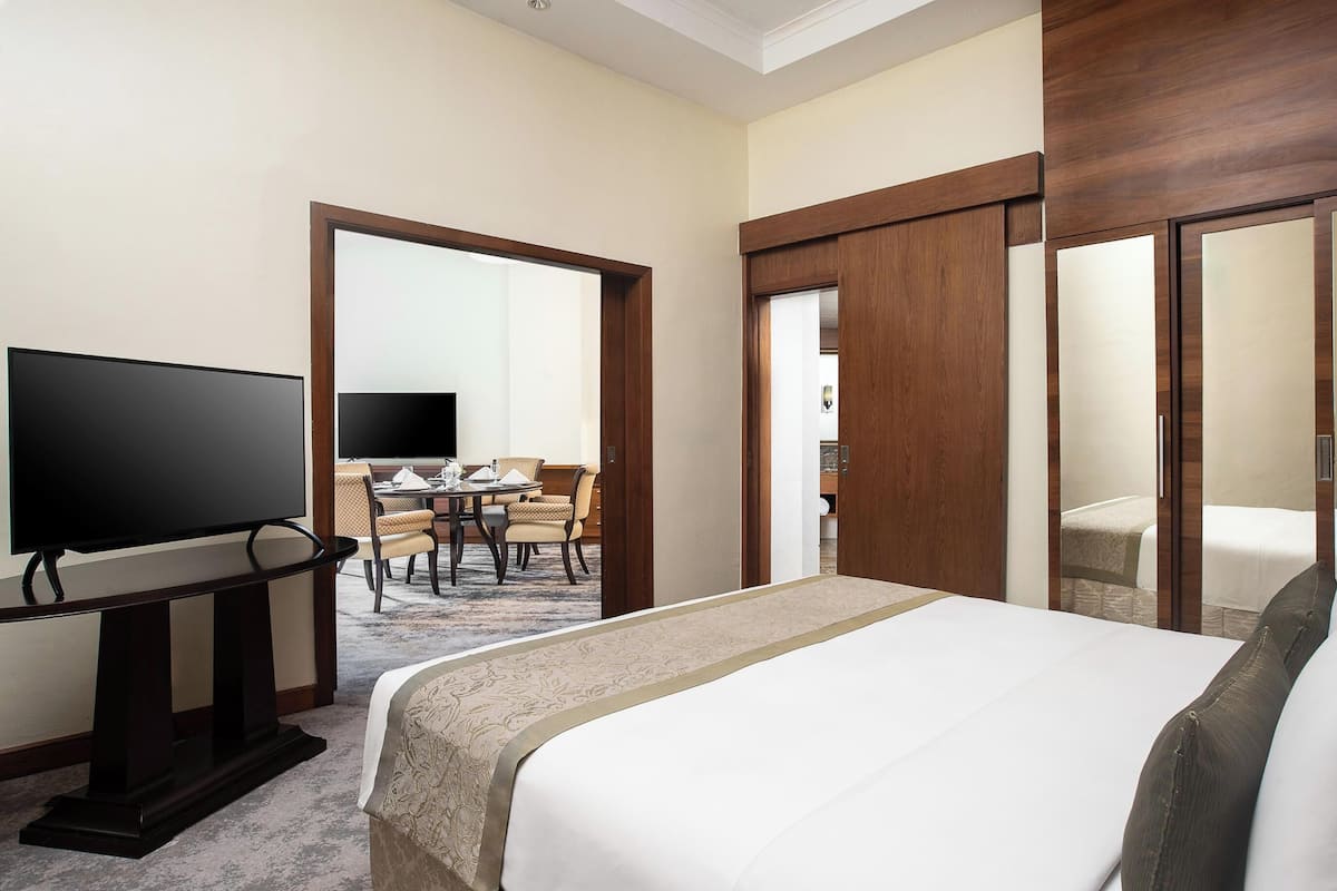 A hotel room with a bed, a television, a dining table with chairs, and a mirror.