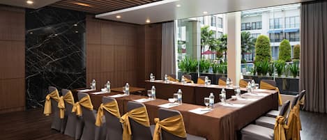 A conference room with a long table, chairs with yellow sashes, and a view of greenery through large windows.