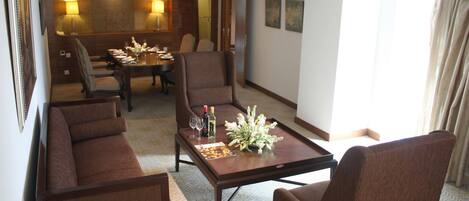 Une chambre d’hôtel comprenant un coin repas, un ensemble de canapés et une table basse agrémentée d’un arrangement floral.