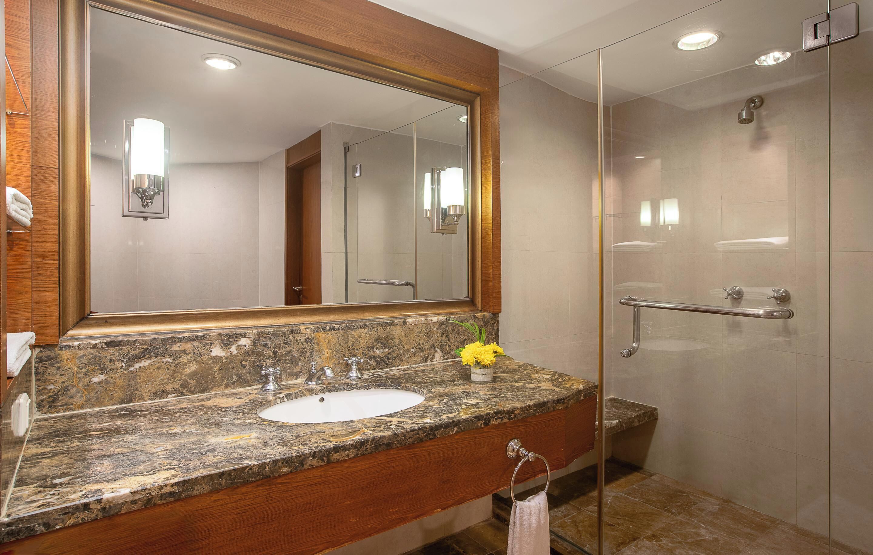 A bathroom with a marble sink, a large mirror, a glass shower enclosure, and a towel rack.