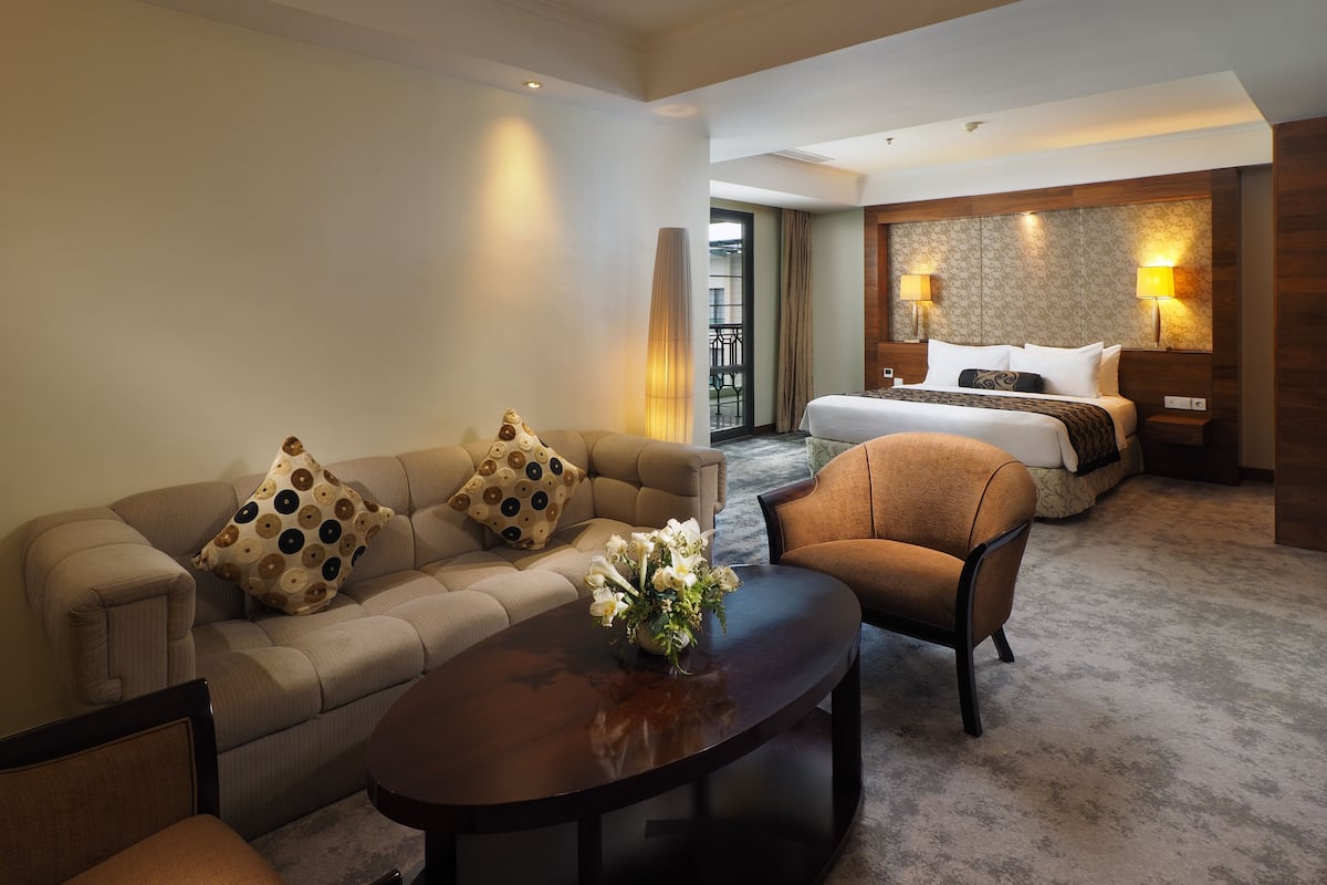 A hotel room with a sofa, armchair, and a bed with a headboard.