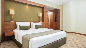 A hotel room with a large bed, wooden headboard, two bedside lamps, and a door leading to another room.