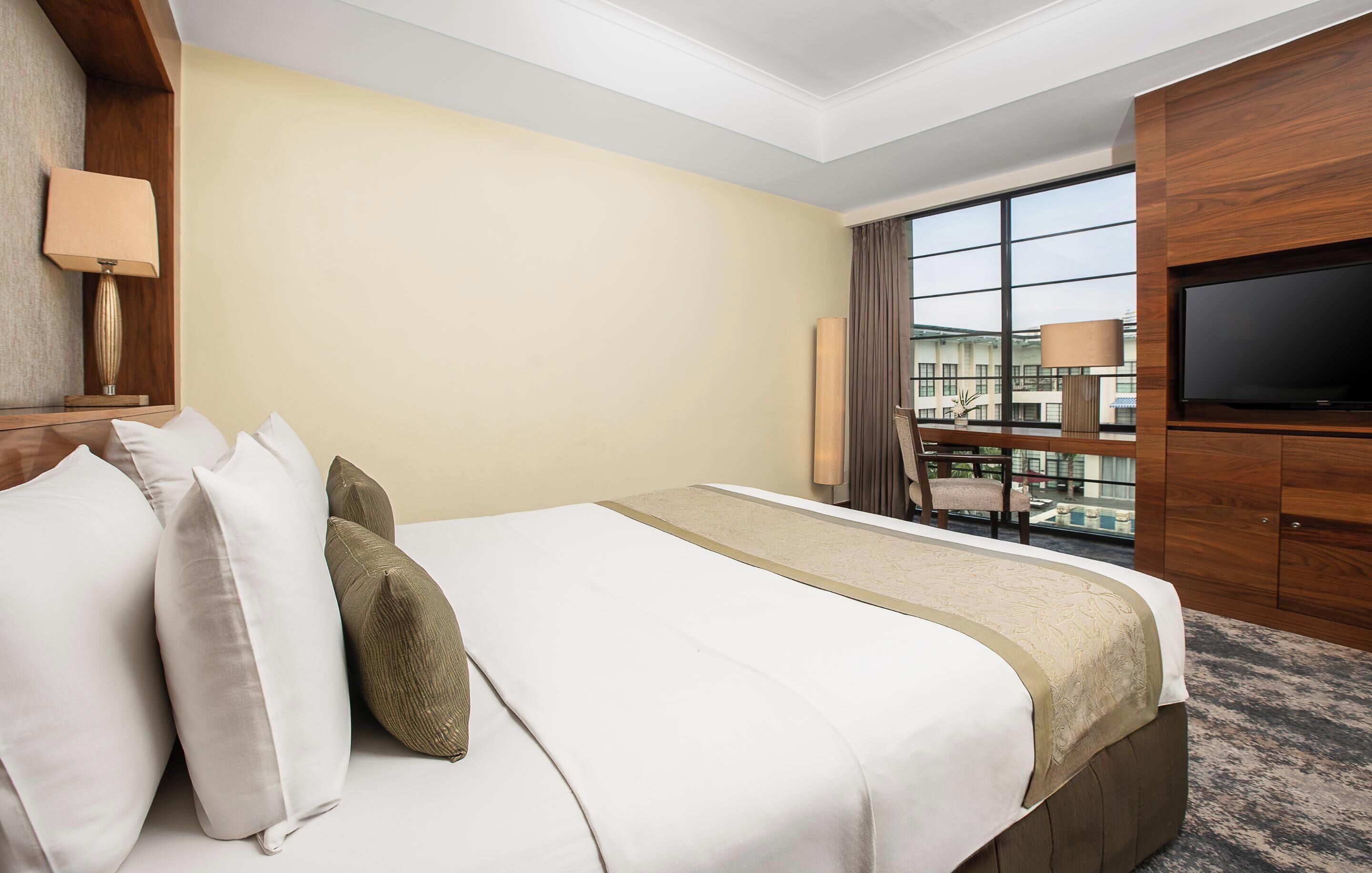 A hotel room with a bed, a TV, a window with a view, and a lamp.