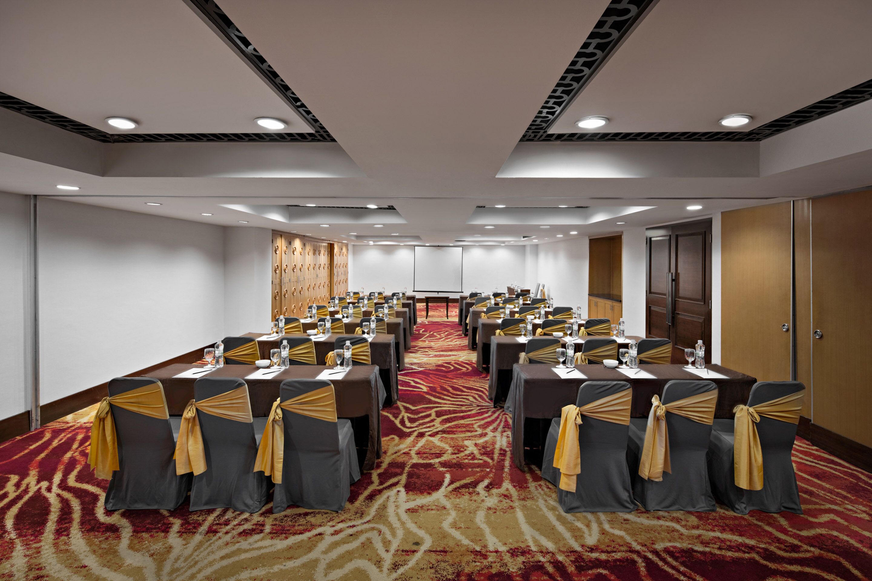 A conference room with a long table, chairs with yellow sashes, and a red carpet.