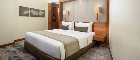 A hotel room with a large bed, wooden headboard, two bedside lamps, and a carpeted floor.