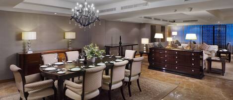 A spacious dining area with a chandelier, a large dining table set for six, and a sofa in the background.