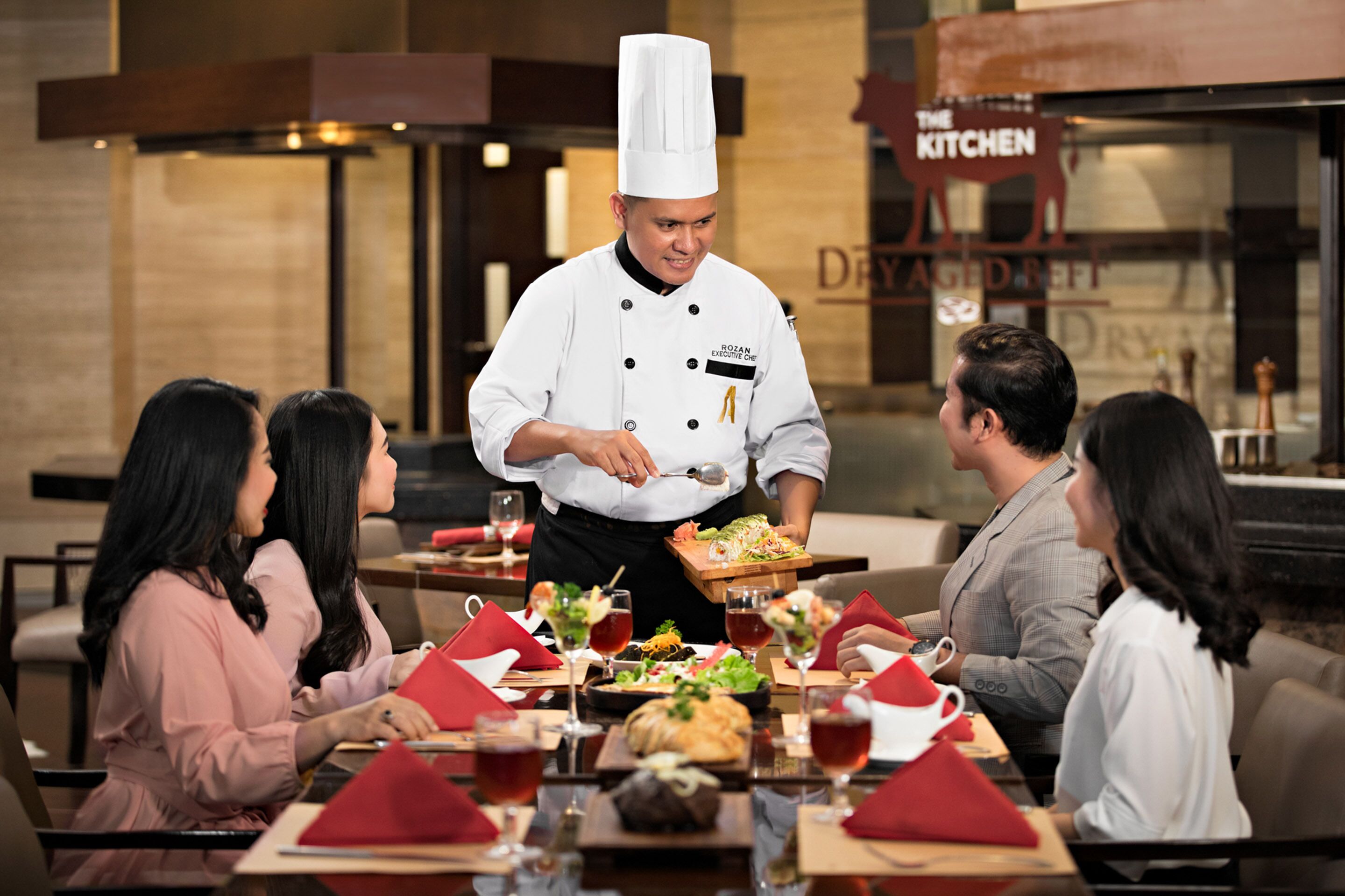 A restaurant setting with a chef serving food to guests.