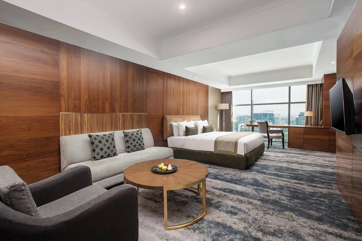 A modern hotel room with a sofa, a round coffee table, a bed, and a TV.