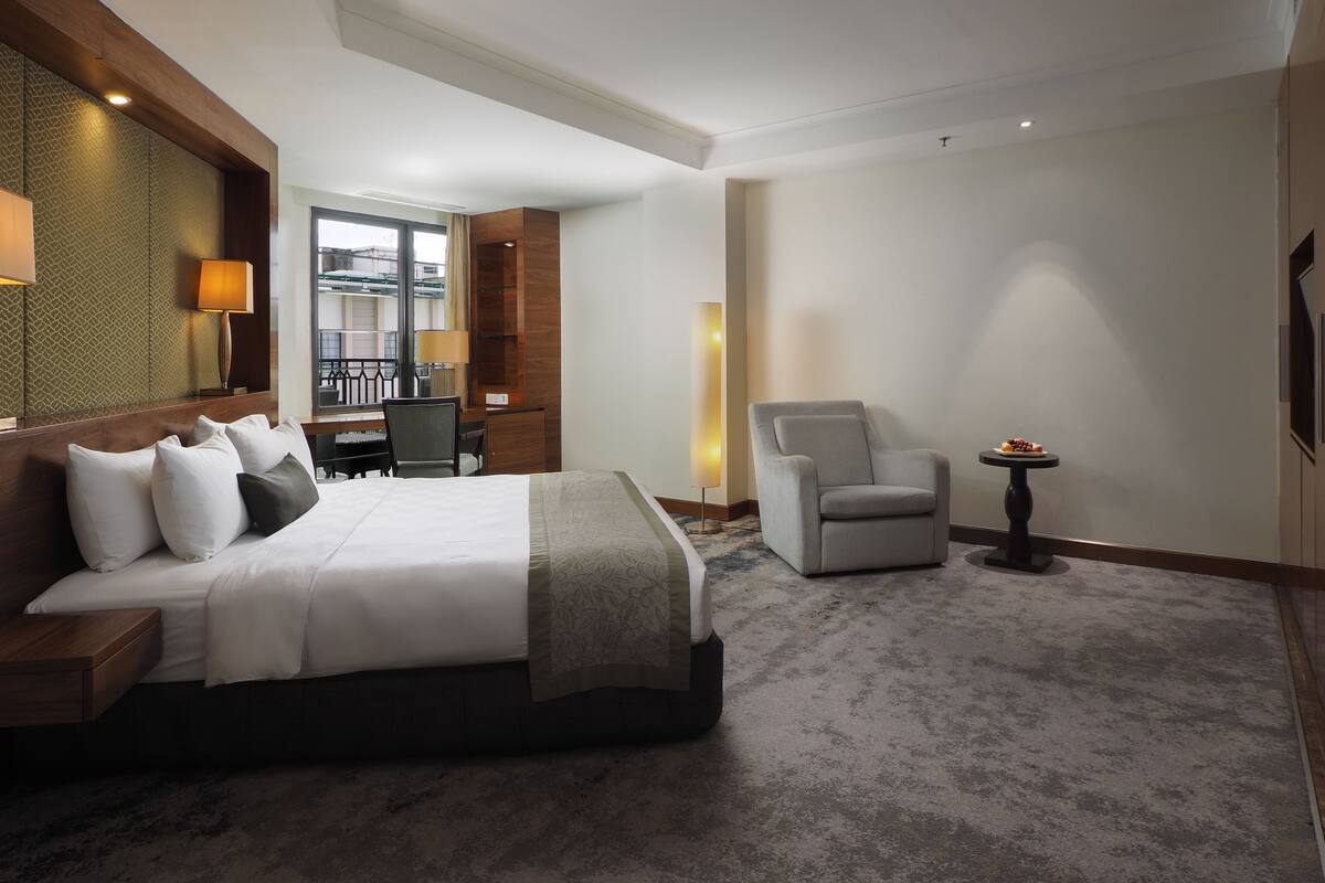 A hotel room with a large bed, a desk, a chair, and a small table with a decorative item.