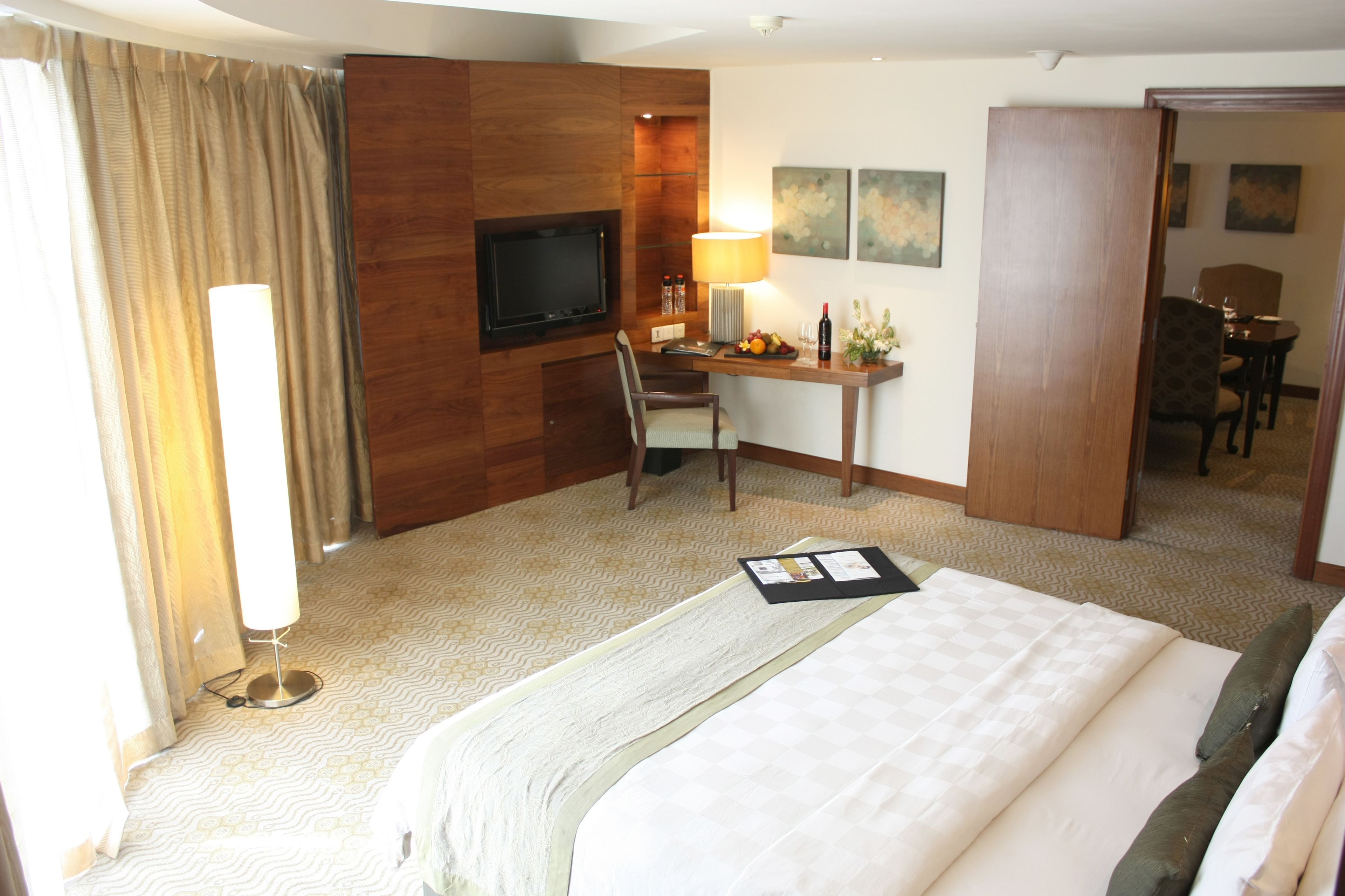 A hotel room with a bed, a desk with a computer, a TV, and a dining area with chairs and a table.