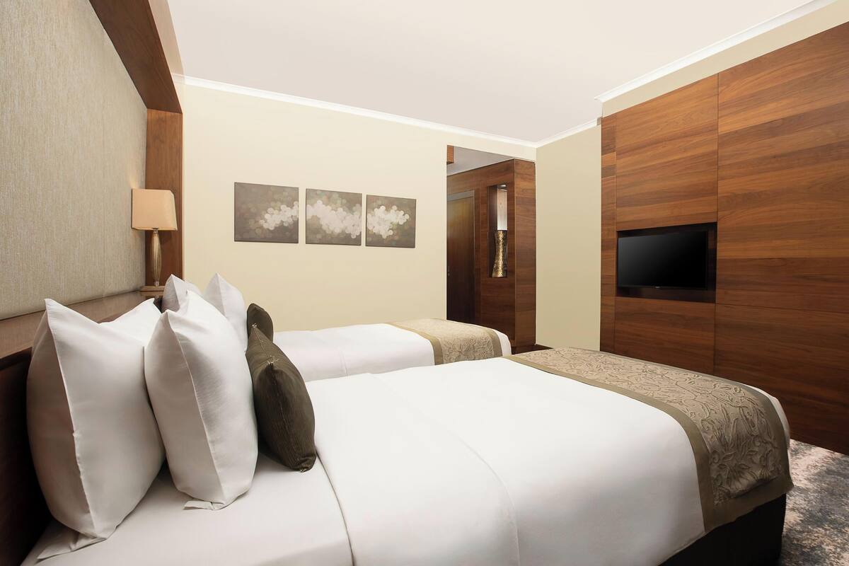 A hotel room with two beds, a TV, and a wooden panel wall.