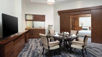 A hotel room with a TV, a dining table set for four, a large mirror, a wardrobe, and a bed.