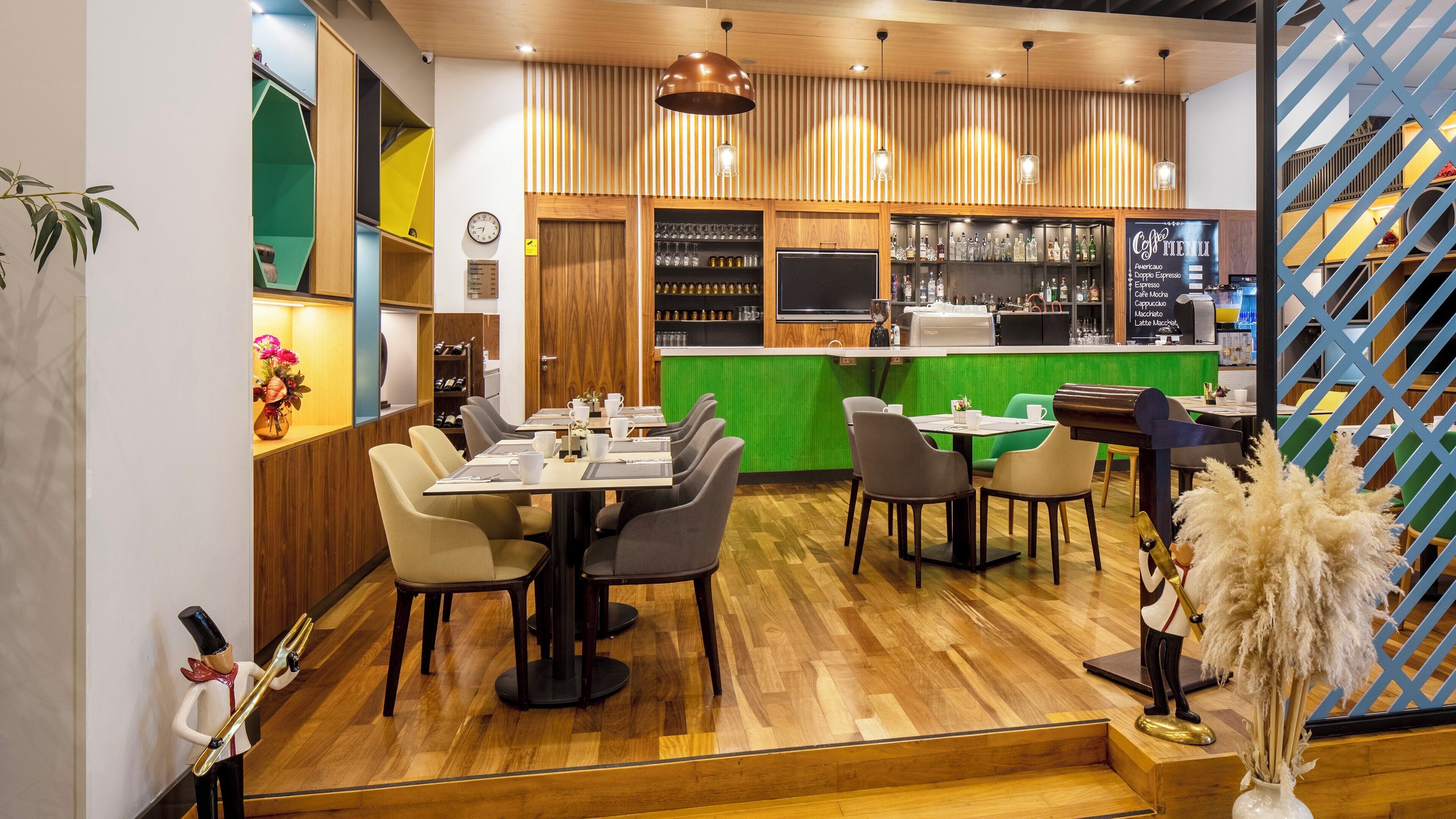 A modern cafe with wooden flooring, green accents, and a variety of seating options.