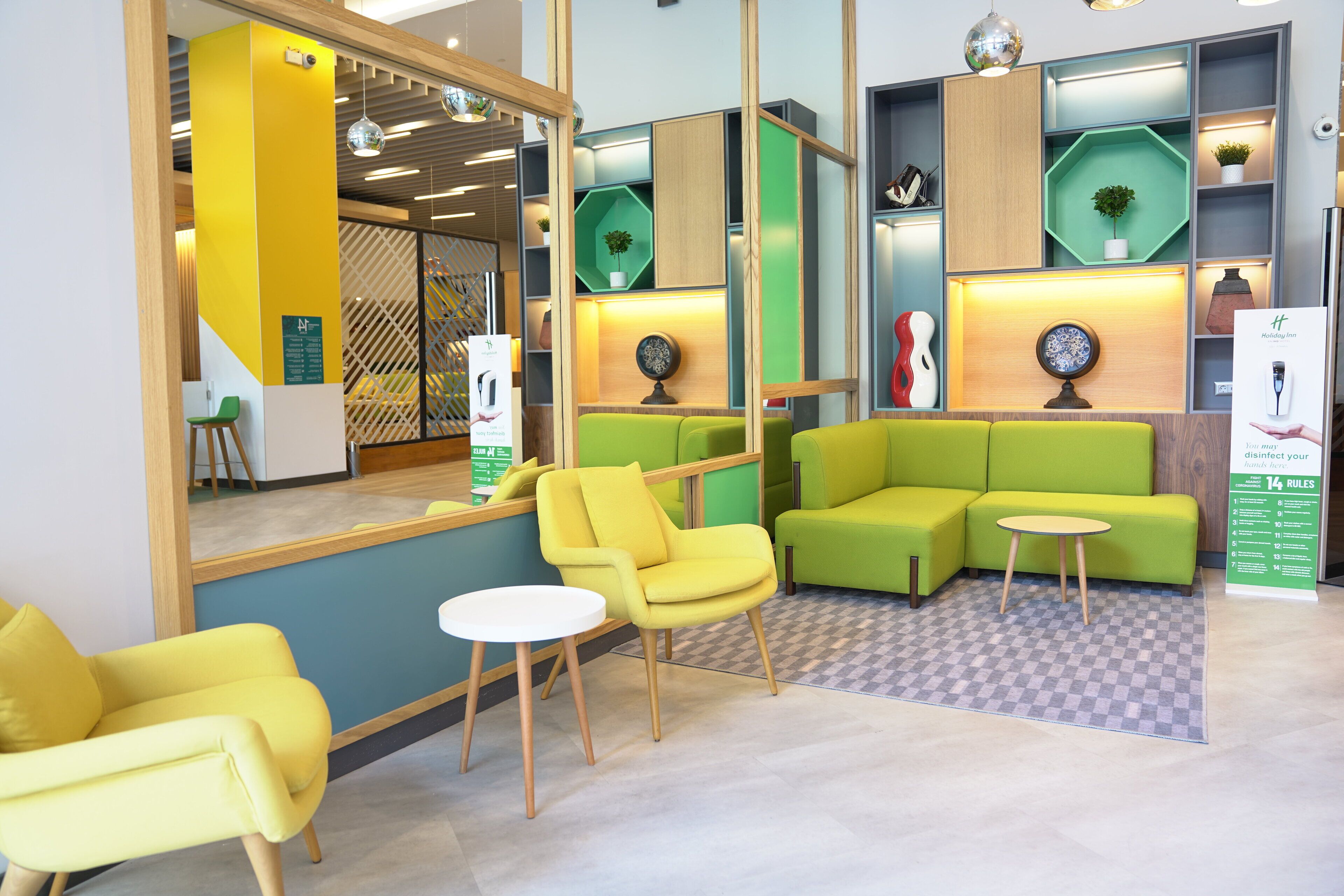 Una zona de recepción moderna con asientos verdes y amarillos, suelo a cuadros y un mostrador de recepción con un letrero verde.