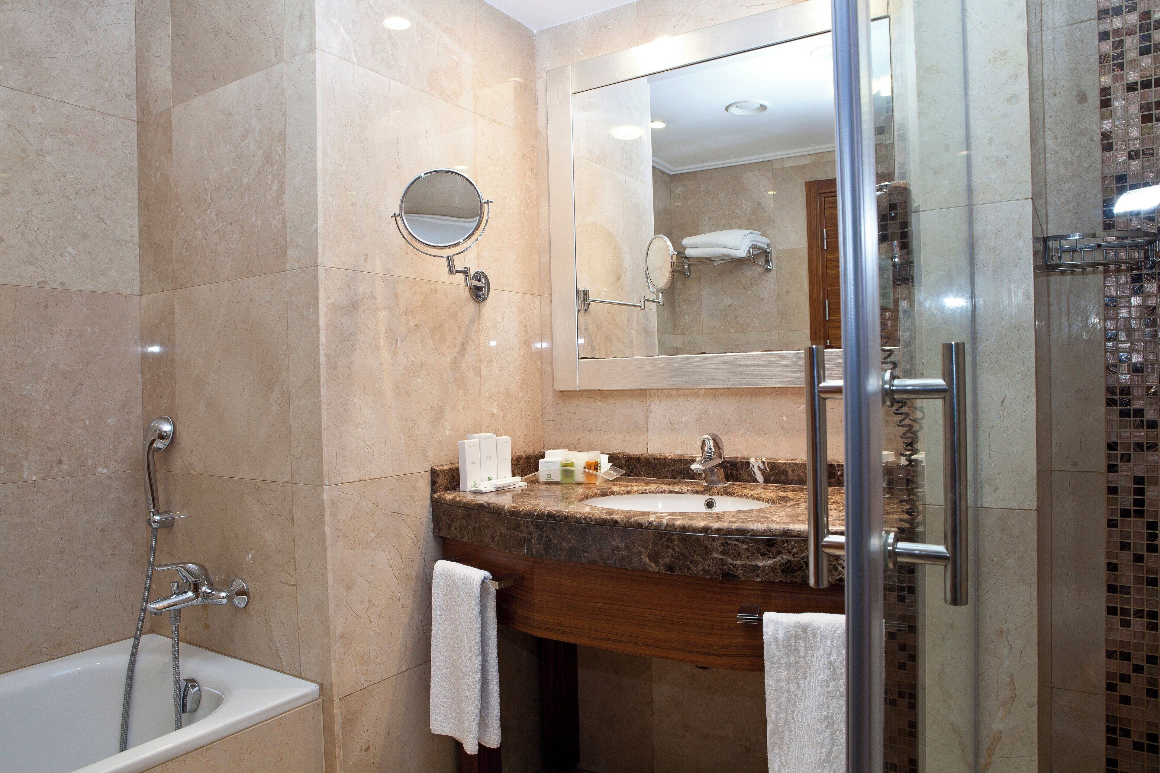 A modern bathroom with a marble sink, a glass-enclosed shower, and a large mirror.