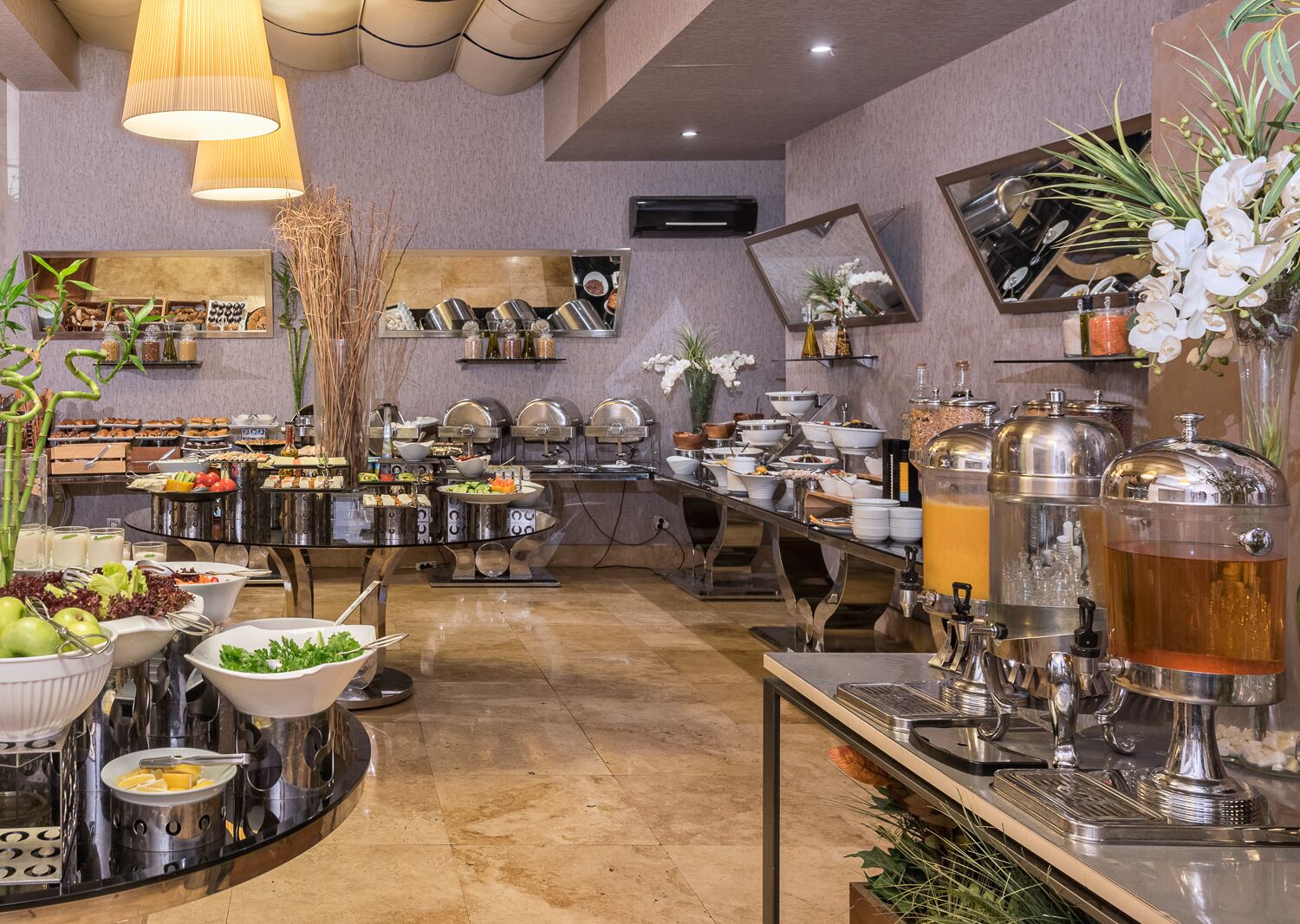 A buffet setup with various food stations, including a fruit bowl, salad, and multiple beverage dispensers.