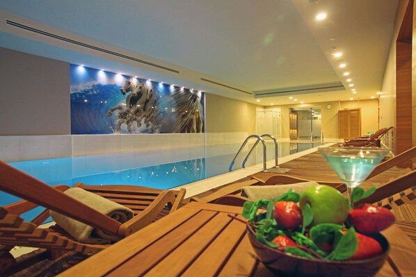Un espace piscine avec des chaises longues en bois, un panier de fruits et une fresque murale.