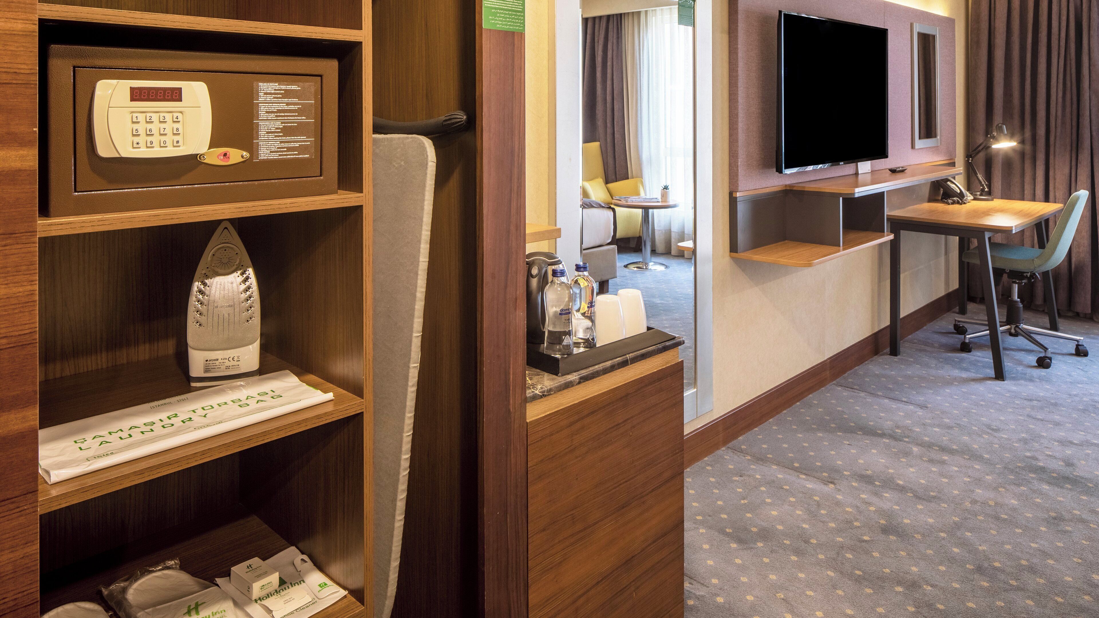 A hotel room with a desk, chair, television, and a minibar.