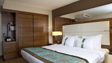 A hotel room with a large bed, wooden wardrobe, bedside table with a lamp, and a mirror above the bed.