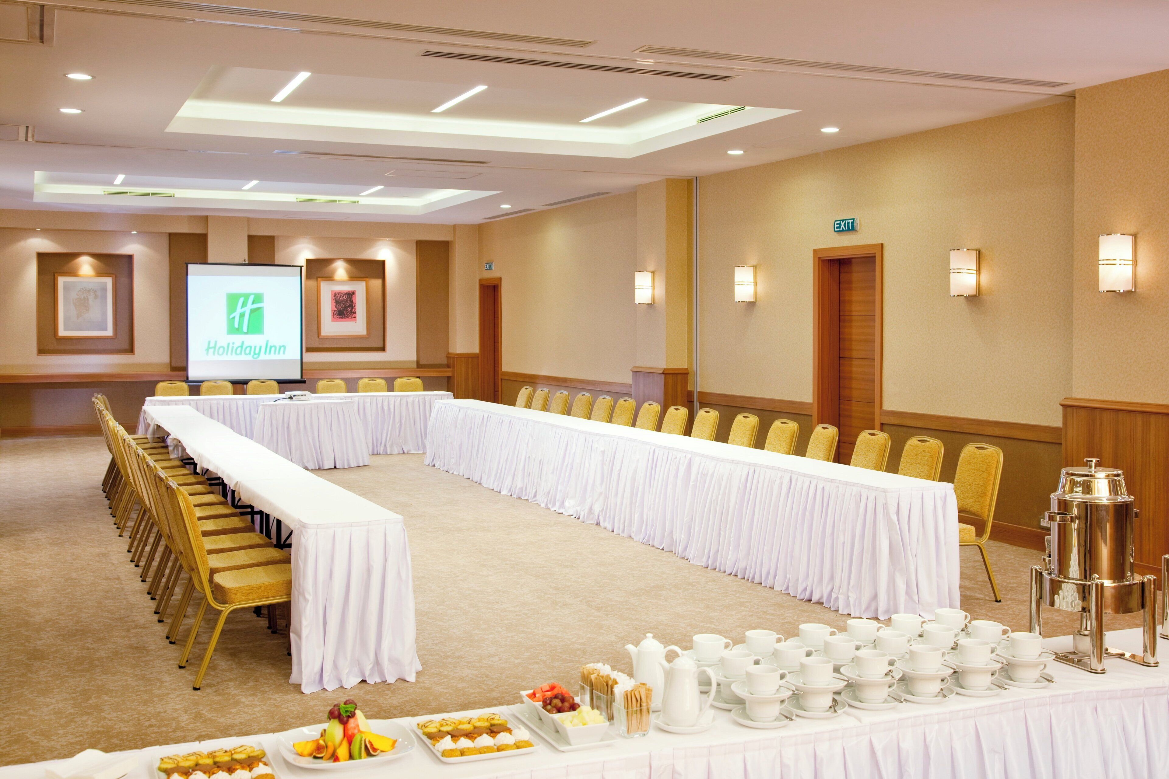 A conference room with a long table, chairs, and a screen displaying the Holiday Inn logo.