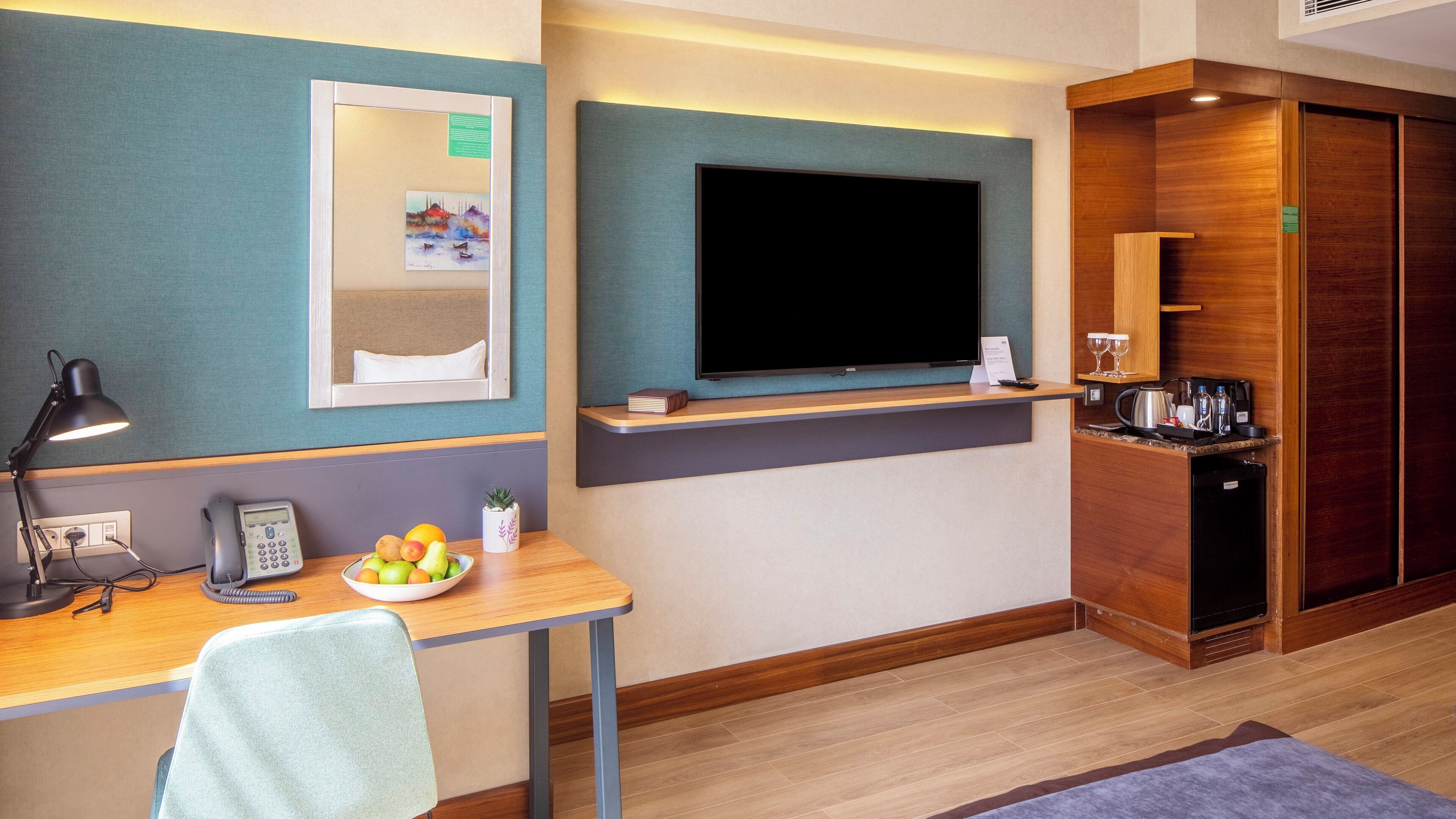 A hotel room with a desk, chair, telephone, and a television on a stand.