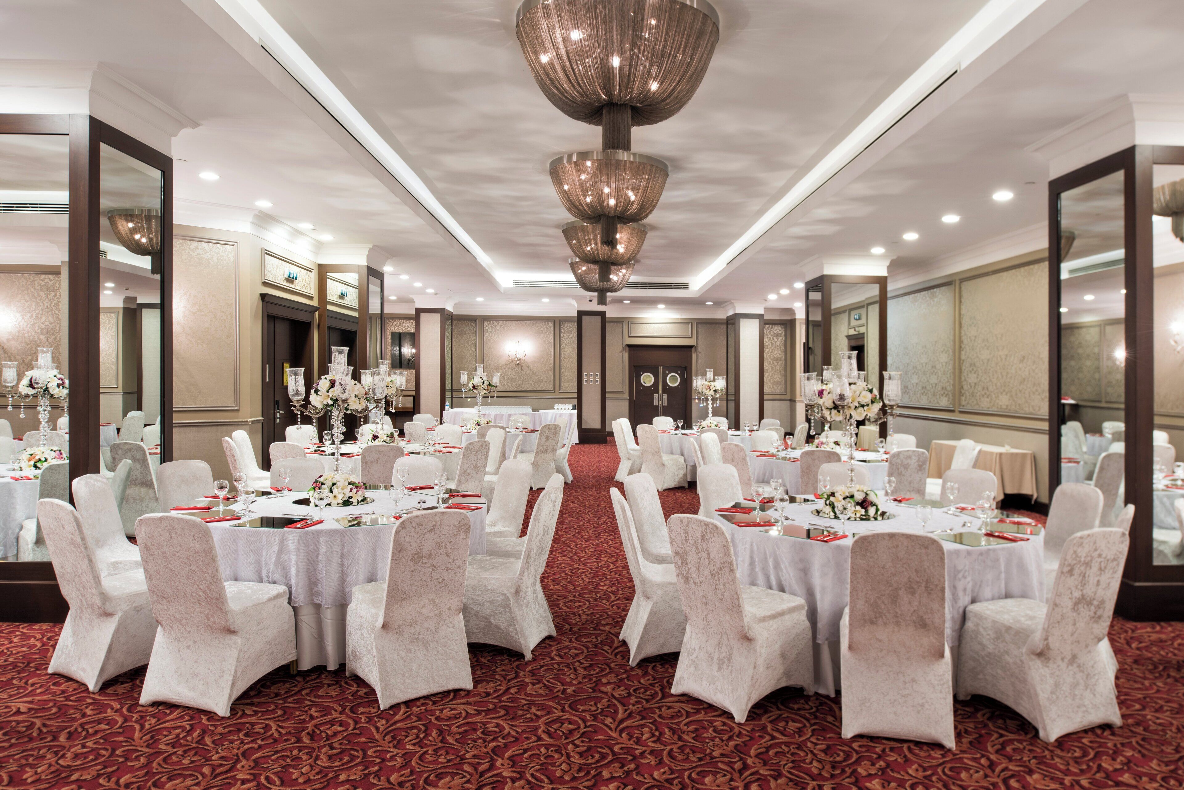 A banquet hall with round tables, white chairs, and floral centerpieces.