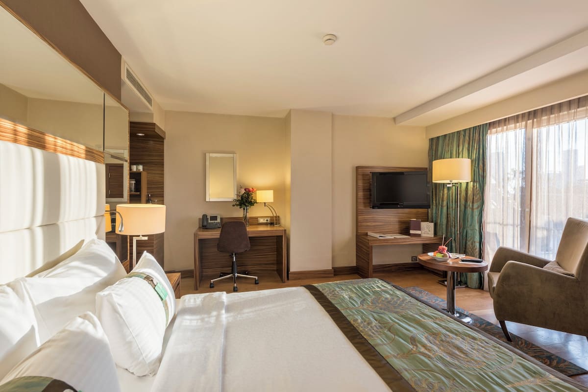 A hotel room with a large bed, a desk with a chair, a television, and a seating area with a chair.