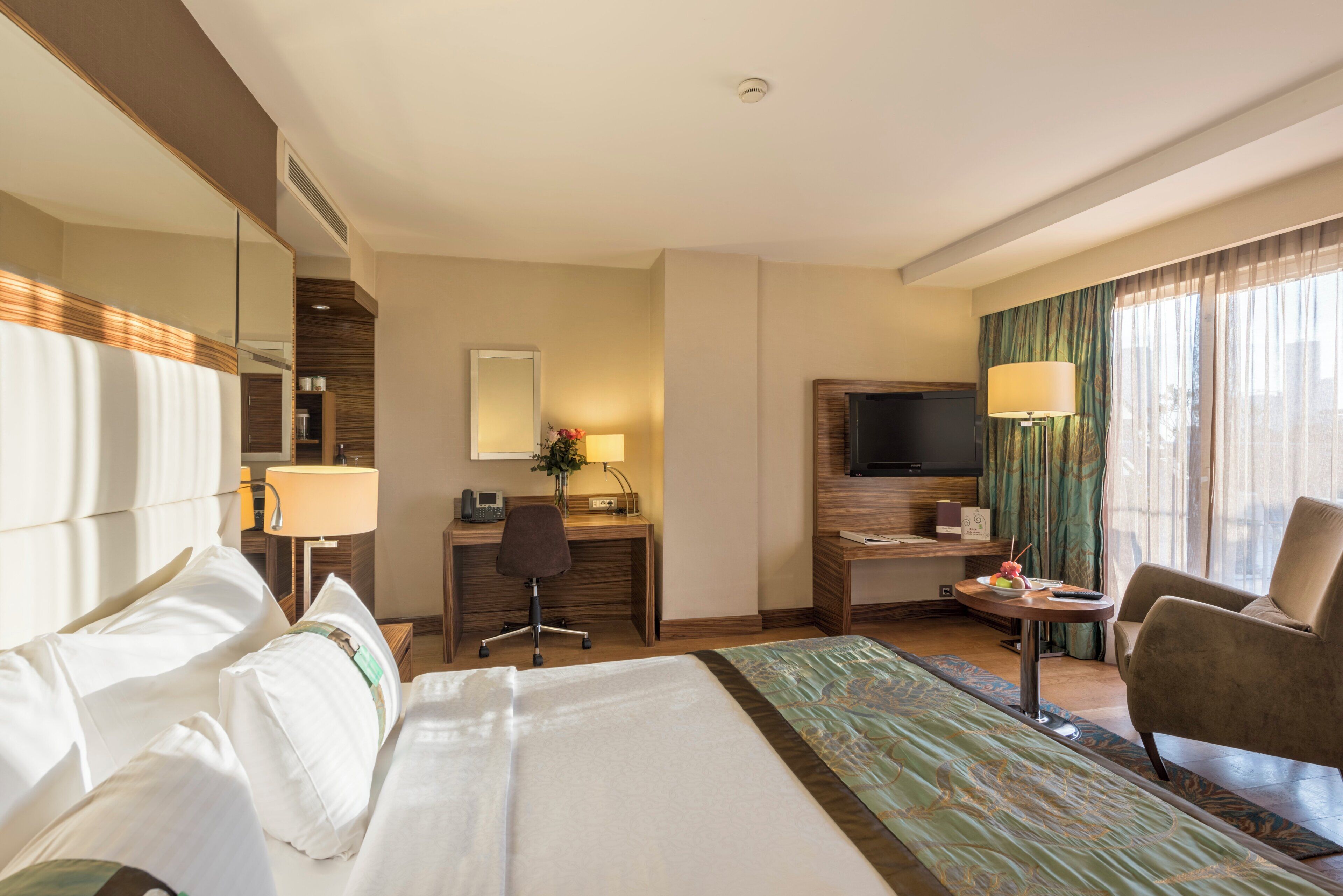 A hotel room with a large bed, a desk with a chair, a television, and a seating area with a chair.