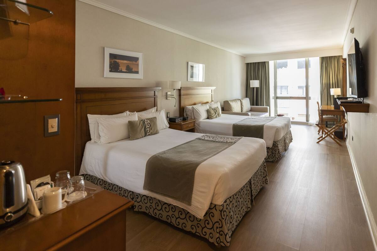 A hotel room with two beds, a desk, a chair, a TV, and a window with curtains.