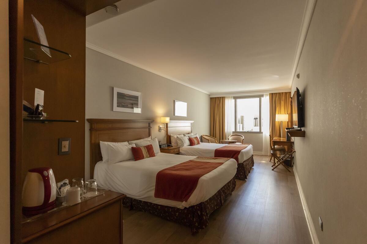A hotel room with two beds, a desk, a chair, a television, and a window with curtains.