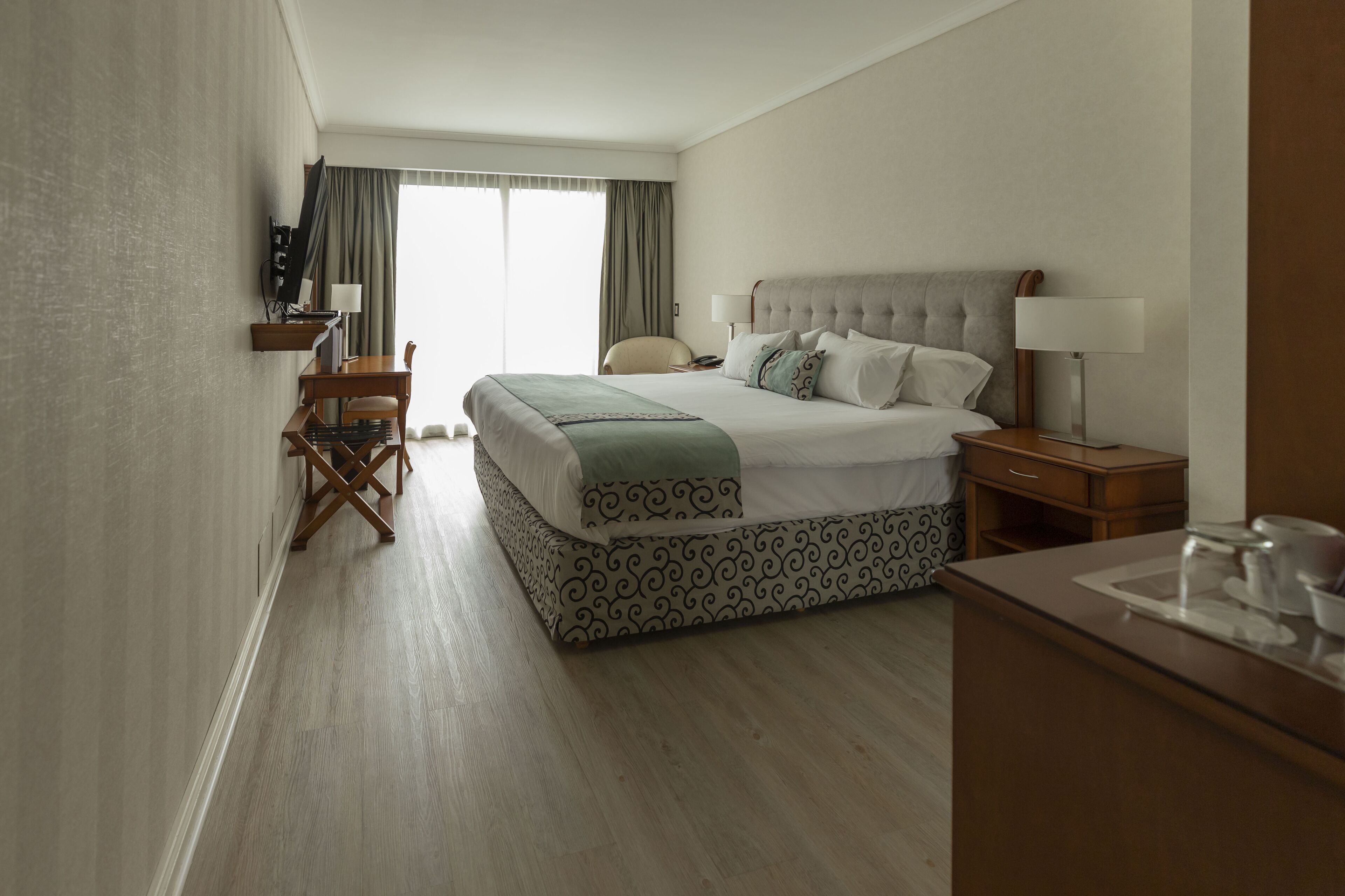 A hotel room with a large bed, a desk, a chair, and a television.