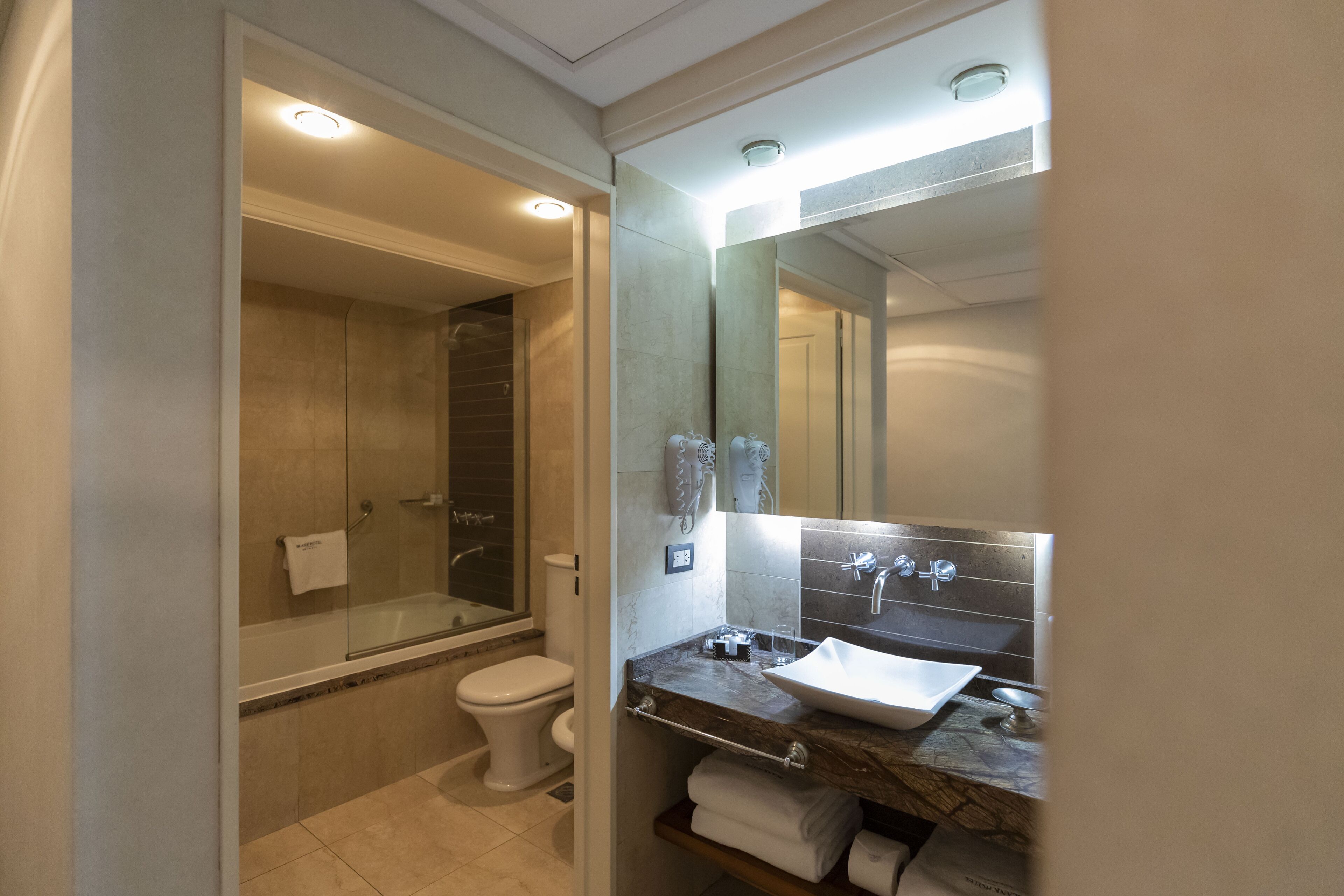 Un baño moderno con ducha cubierta por vidrio, inodoro blanco y lavamanos de mármol con espejo arriba.