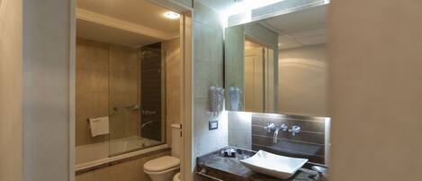 A modern bathroom with a glass-enclosed shower, a white toilet, and a marble countertop sink with a mirror above.