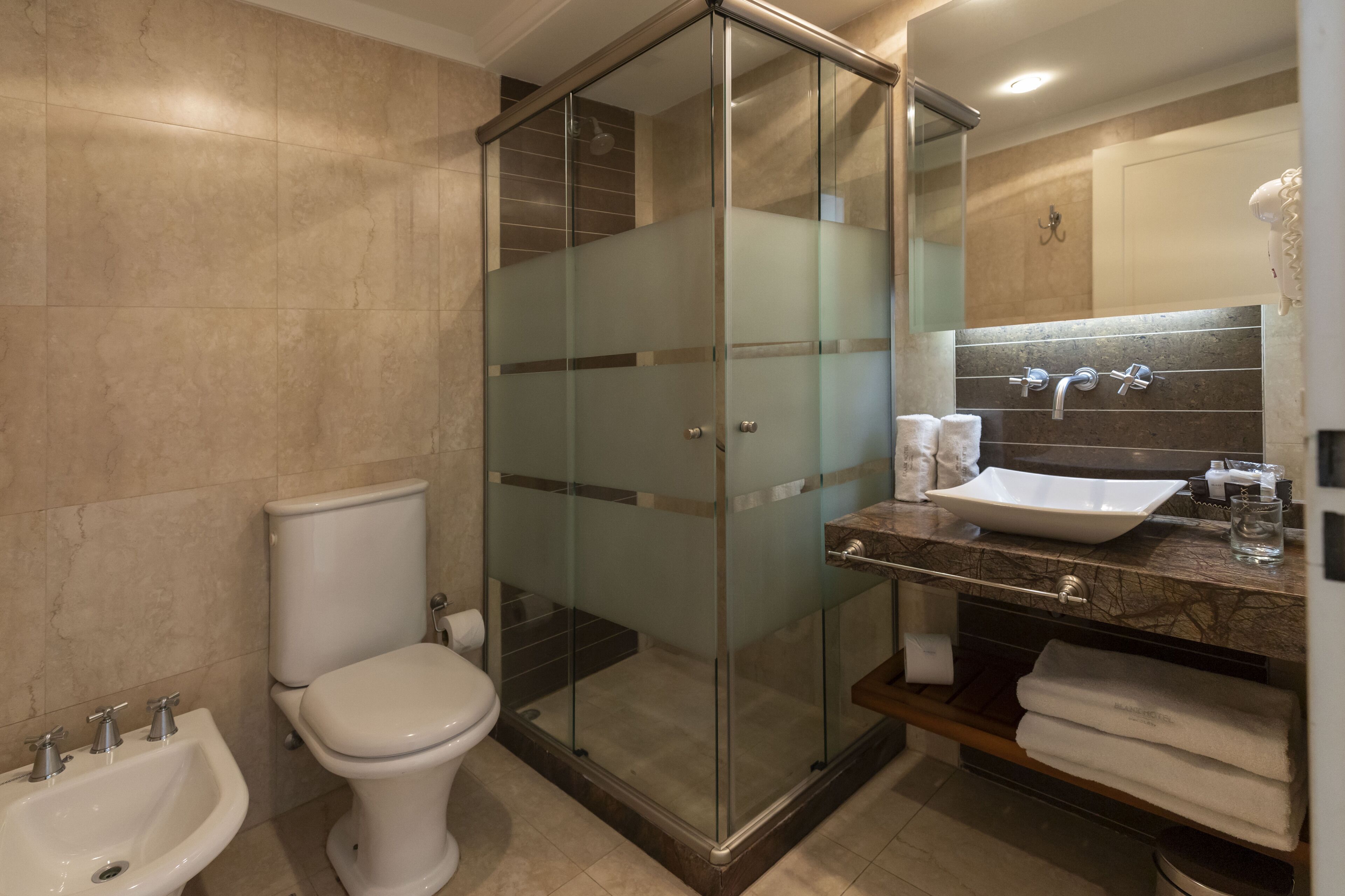 Un baño moderno con ducha de vidrio, inodoro blanco, lavamanos con encimera de mármol y espejo sobre el lavamanos.