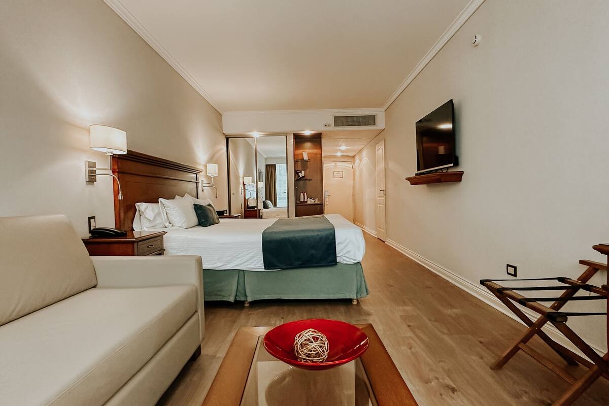 A hotel room with a bed, a sofa, a TV, and a wooden chair.