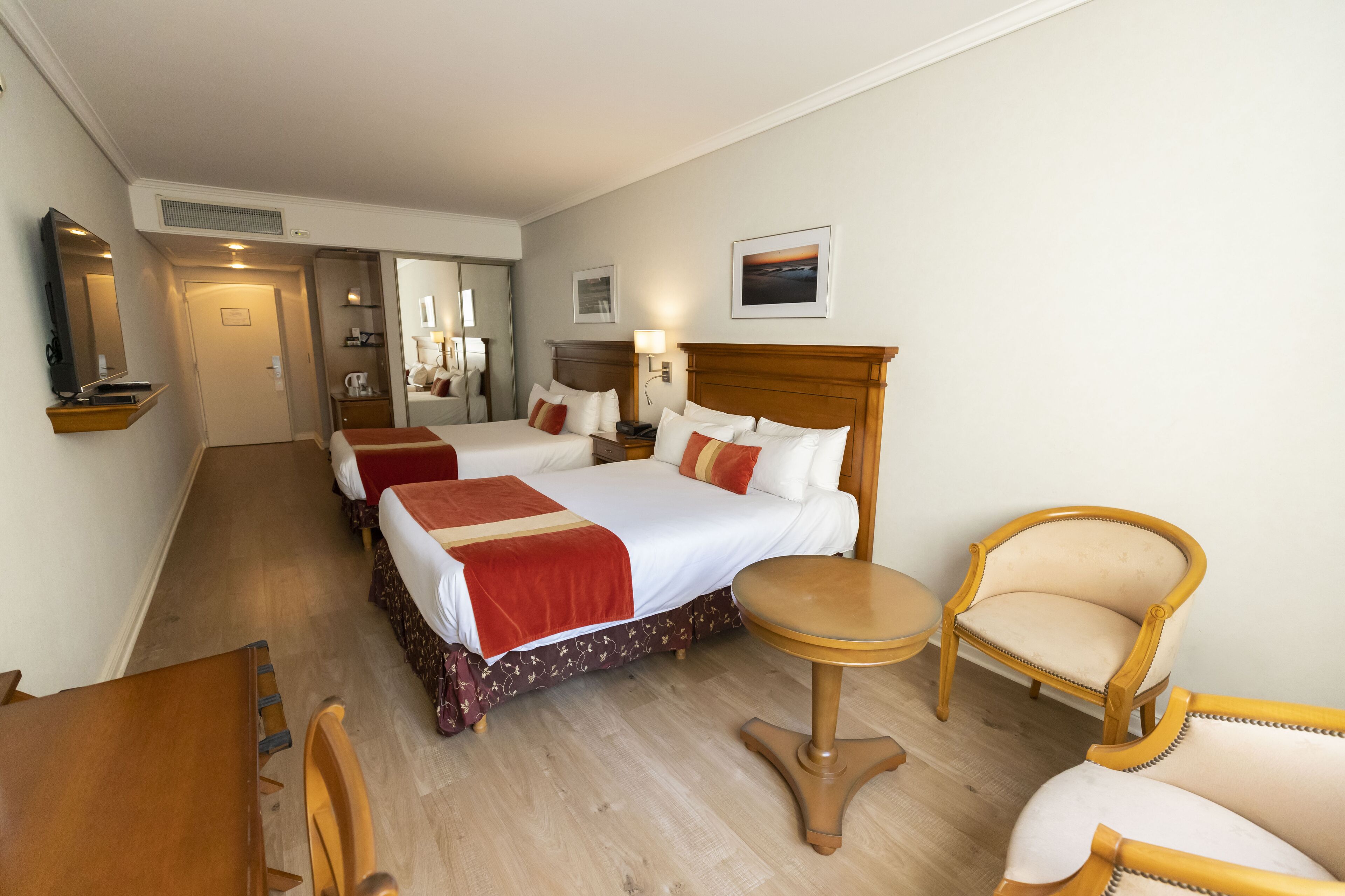 Una habitación de hotel con una cama grande, dos mesitas de noche, una pequeña mesa redonda y dos sillones.