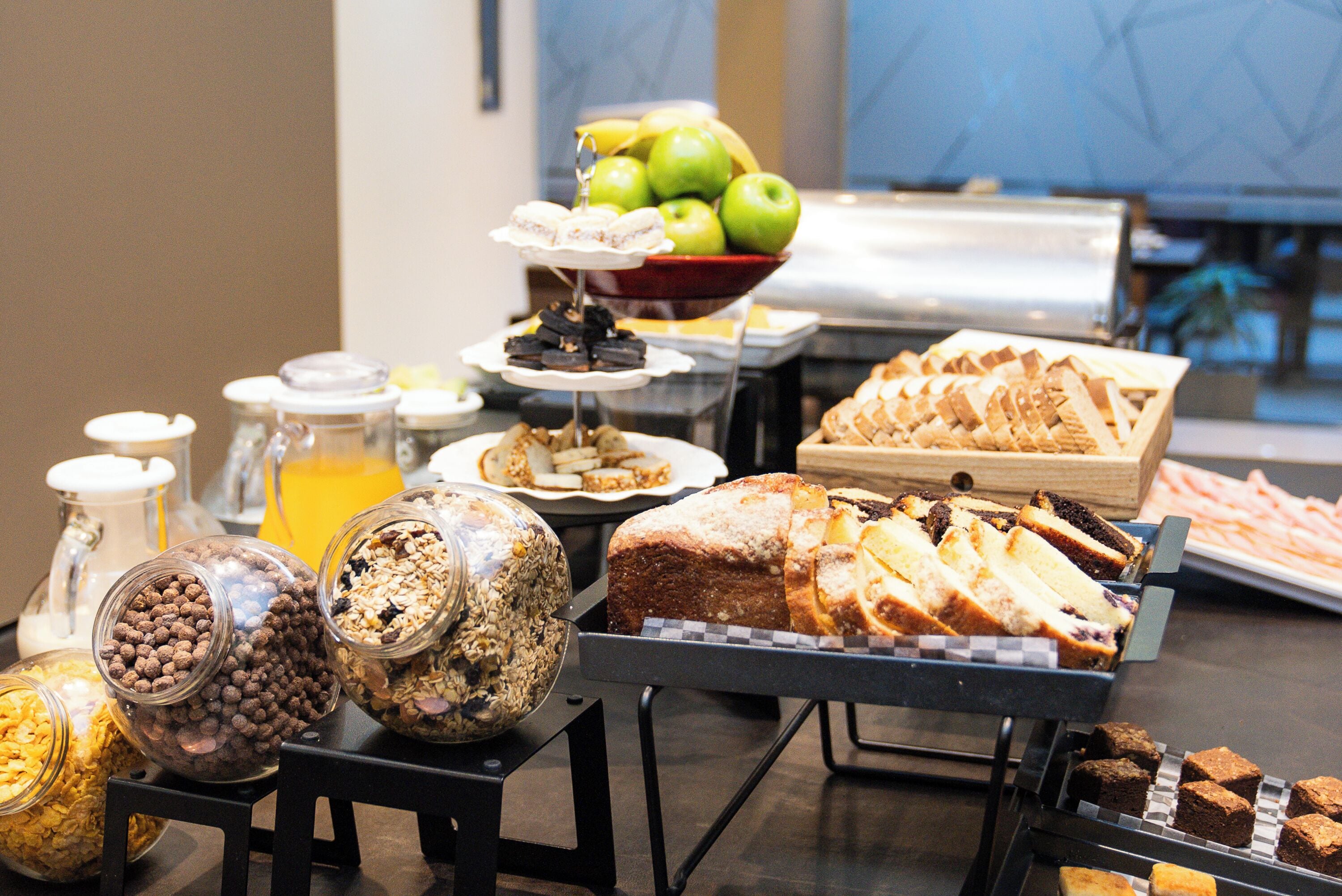 A buffet with various food items including fruits, pastries, and cereals.