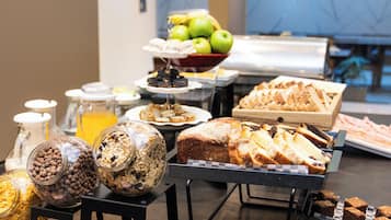 A buffet with various food items including fruits, pastries, and cereals.